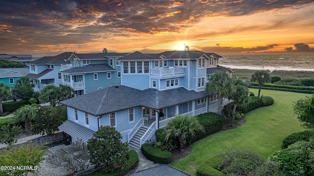 view of front of property featuring a water view, a balcony, and a lawn