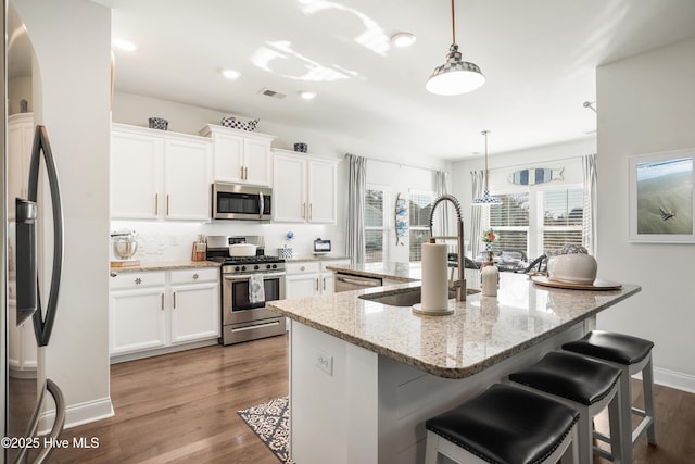 kitchen featuring pendant lighting, light stone countertops, white cabinetry, and stainless steel appliances