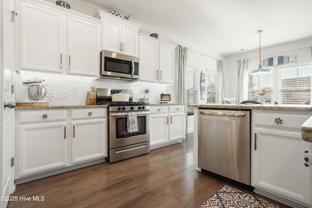 kitchen with hanging light fixtures, white cabinetry, appliances with stainless steel finishes, and light stone counters