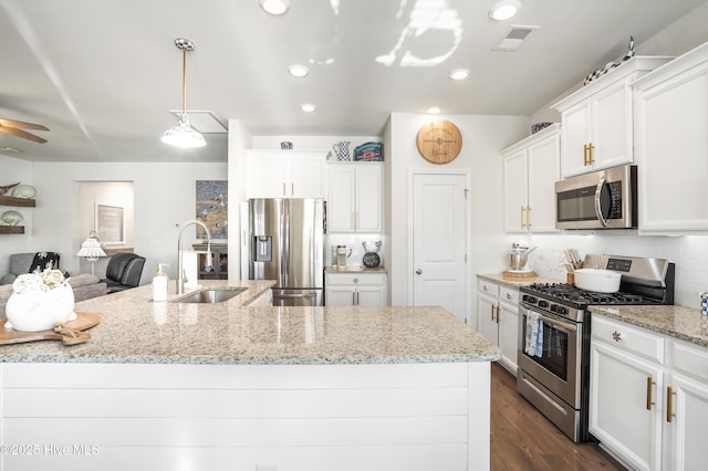 kitchen with appliances with stainless steel finishes, white cabinetry, sink, decorative backsplash, and light stone countertops