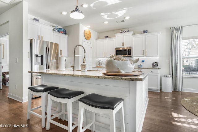 kitchen with appliances with stainless steel finishes, dark hardwood / wood-style flooring, a kitchen island with sink, and white cabinets