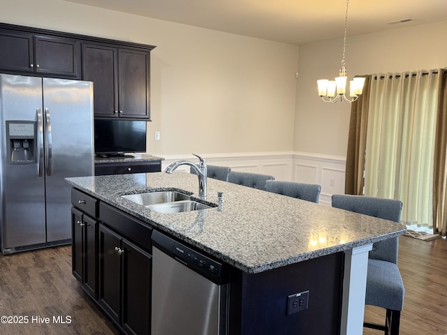 kitchen with sink, appliances with stainless steel finishes, light stone countertops, a center island with sink, and dark hardwood / wood-style flooring