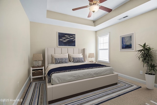 carpeted bedroom with a tray ceiling and ceiling fan