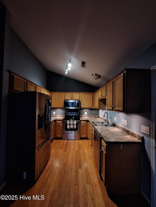 kitchen with vaulted ceiling, appliances with stainless steel finishes, sink, and light hardwood / wood-style flooring