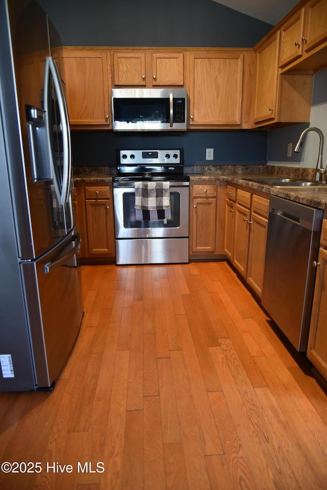 kitchen featuring vaulted ceiling, appliances with stainless steel finishes, sink, and light hardwood / wood-style floors