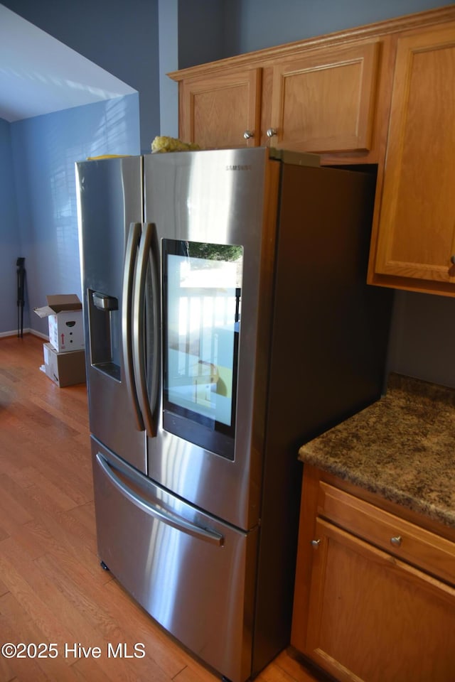 kitchen with dark stone counters, stainless steel fridge with ice dispenser, and light wood-type flooring