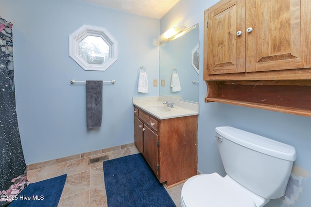 bathroom featuring baseboards, visible vents, toilet, stone finish floor, and vanity