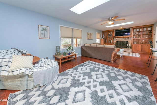 living room with a skylight, wood-type flooring, ceiling fan, a brick fireplace, and built in shelves