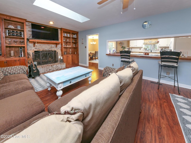 living room featuring built in shelves, a skylight, dark hardwood / wood-style floors, ceiling fan, and a fireplace