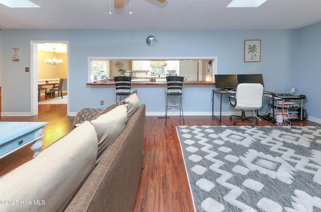 living area featuring a skylight, baseboards, dark wood-style flooring, and ceiling fan with notable chandelier