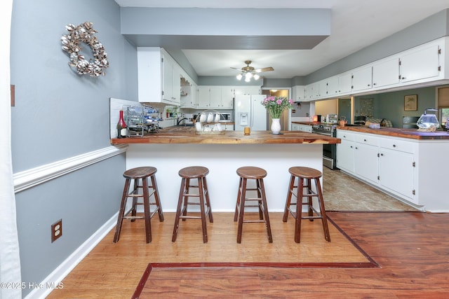 kitchen with white fridge with ice dispenser, white cabinets, a breakfast bar, and kitchen peninsula