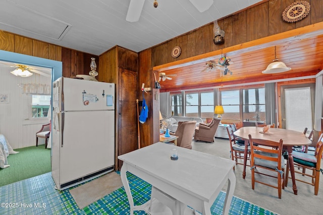 kitchen featuring white refrigerator, hanging light fixtures, wooden walls, and ceiling fan