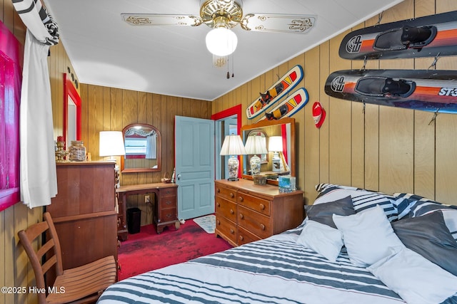 bedroom featuring ceiling fan, wooden walls, and dark colored carpet