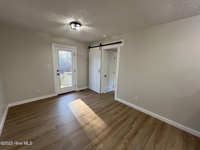 unfurnished bedroom featuring hardwood / wood-style flooring, a barn door, access to outside, and a textured ceiling