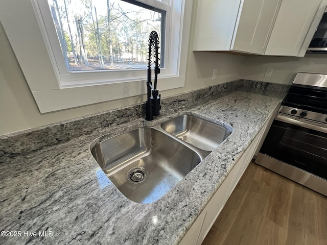 interior details with sink, stainless steel electric range, white cabinetry, dark hardwood / wood-style floors, and light stone counters