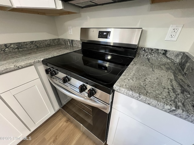 kitchen with light stone counters, stainless steel electric range, light wood-type flooring, white cabinets, and exhaust hood