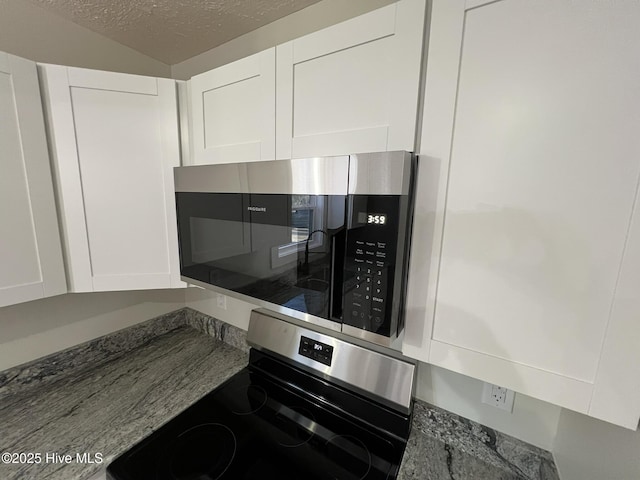 interior details with appliances with stainless steel finishes, dark stone counters, and white cabinets