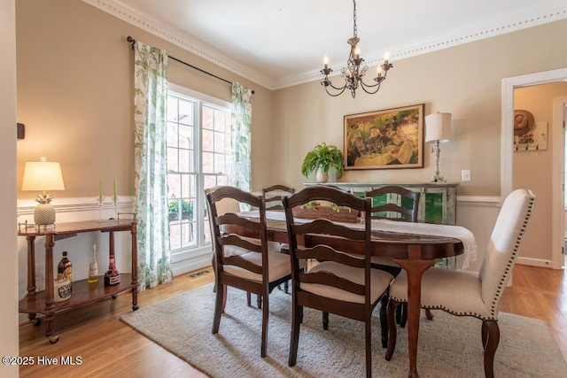 dining space with ornamental molding, a chandelier, and light hardwood / wood-style flooring