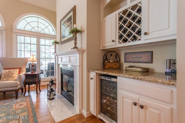 bar featuring white cabinets, a high end fireplace, wine cooler, and light stone counters