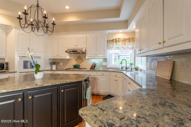 kitchen with sink, white cabinetry, hanging light fixtures, appliances with stainless steel finishes, and stone counters