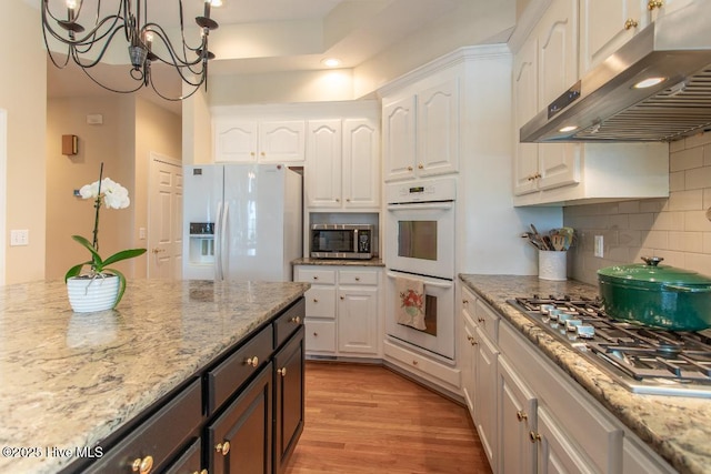 kitchen with extractor fan, white cabinetry, light stone counters, light hardwood / wood-style flooring, and appliances with stainless steel finishes