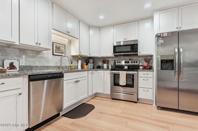 kitchen with appliances with stainless steel finishes, white cabinetry, sink, dark stone countertops, and backsplash