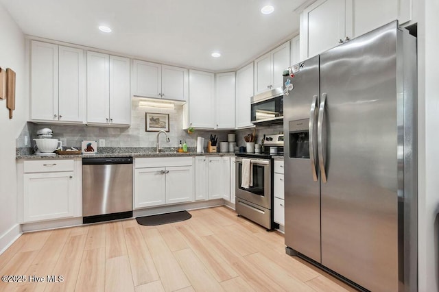 kitchen featuring sink, white cabinetry, stainless steel appliances, tasteful backsplash, and dark stone counters