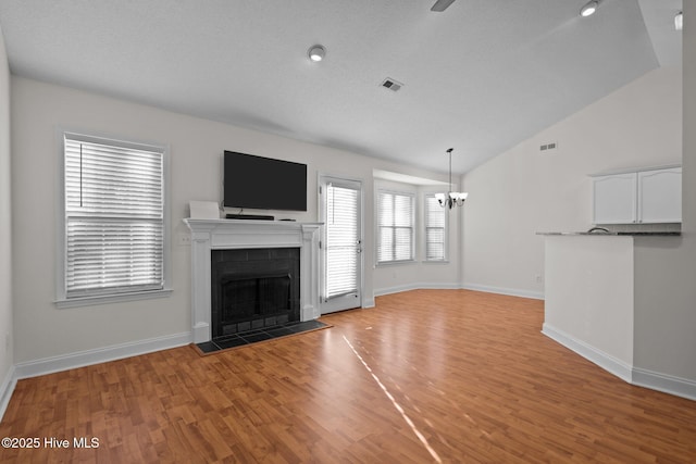 unfurnished living room with a tiled fireplace, a notable chandelier, vaulted ceiling, and light hardwood / wood-style floors