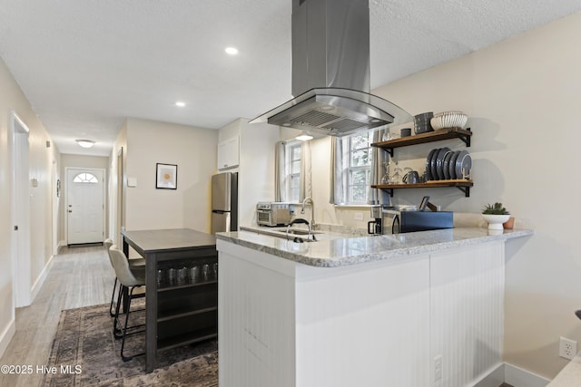kitchen with sink, appliances with stainless steel finishes, white cabinetry, island range hood, and light stone countertops