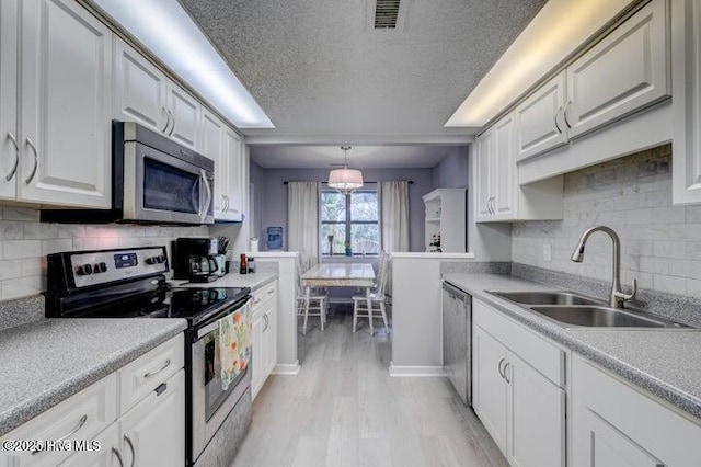 kitchen with sink, appliances with stainless steel finishes, white cabinetry, hanging light fixtures, and light hardwood / wood-style floors