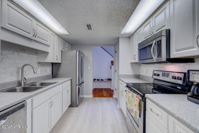 kitchen featuring sink, a textured ceiling, stainless steel appliances, light hardwood / wood-style floors, and white cabinets