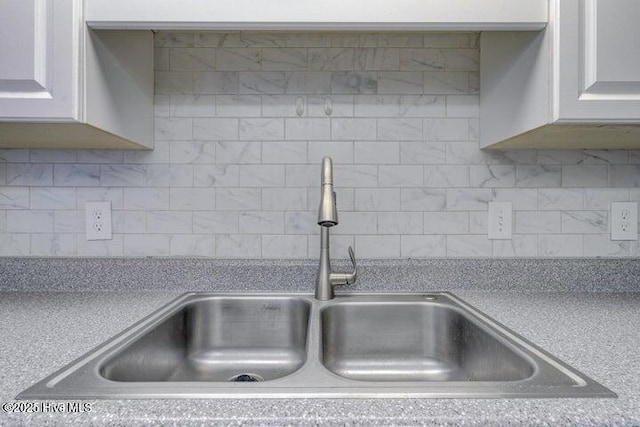 interior details with tasteful backsplash, sink, and white cabinets