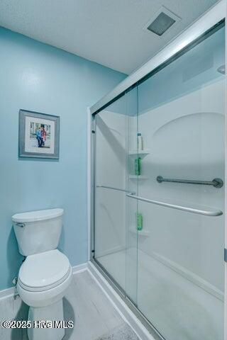 bathroom featuring a shower with door and toilet