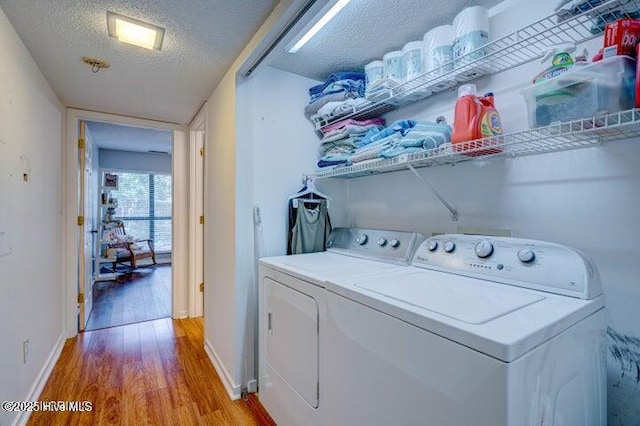 clothes washing area with washing machine and clothes dryer, wood-type flooring, and a textured ceiling