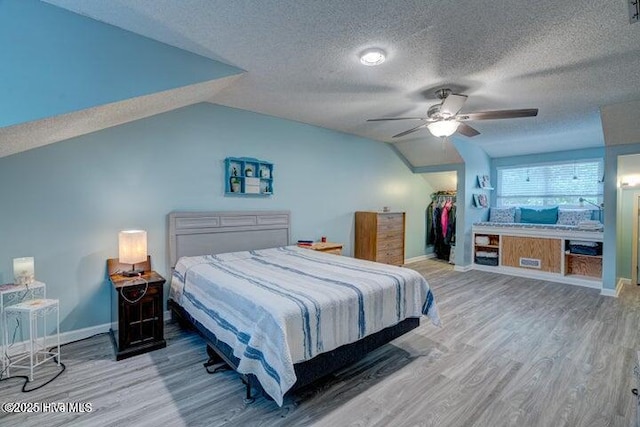 bedroom featuring vaulted ceiling, wood-type flooring, a textured ceiling, a walk in closet, and a closet