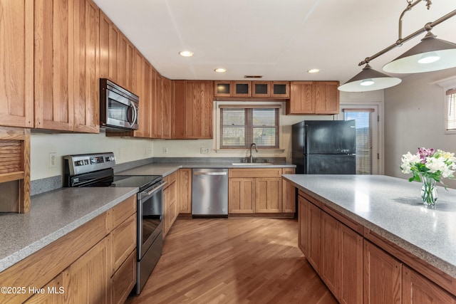 kitchen with stainless steel appliances, a sink, brown cabinetry, glass insert cabinets, and pendant lighting