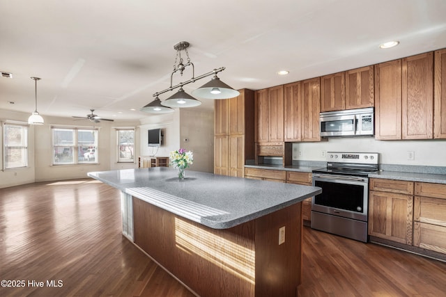 kitchen featuring open floor plan, stainless steel appliances, brown cabinetry, and decorative light fixtures