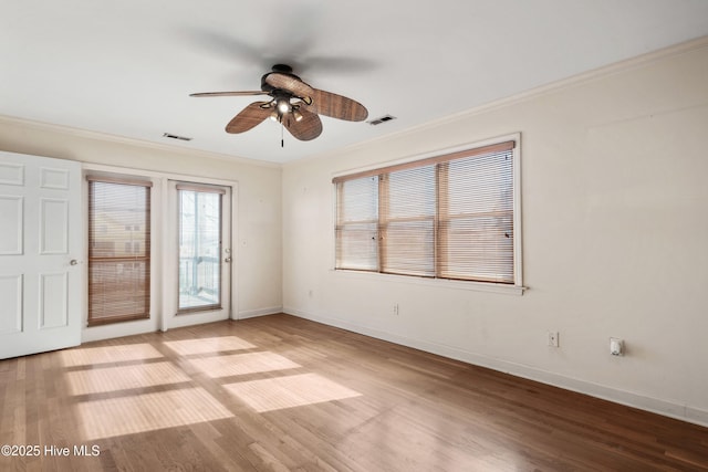 empty room featuring light wood finished floors, baseboards, visible vents, a ceiling fan, and crown molding