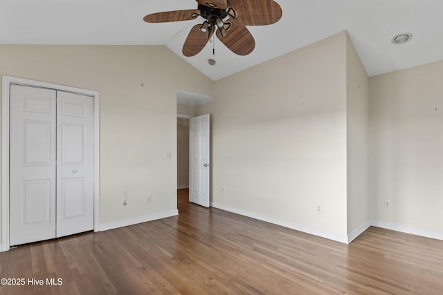 unfurnished bedroom with lofted ceiling, a closet, wood finished floors, and baseboards