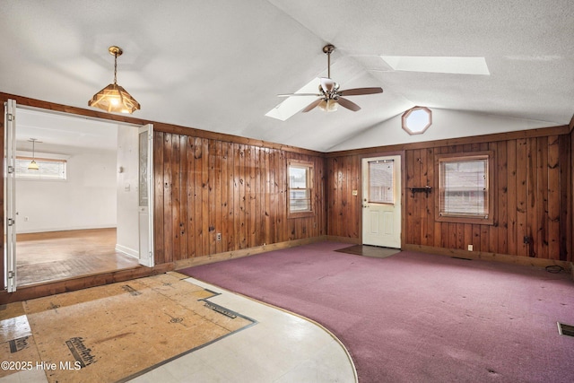 spare room featuring visible vents, a ceiling fan, lofted ceiling with skylight, carpet floors, and wood walls