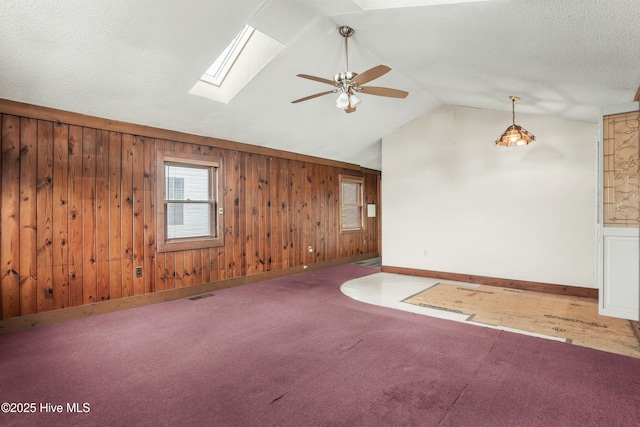 unfurnished living room featuring a textured ceiling, wood walls, visible vents, lofted ceiling with skylight, and carpet