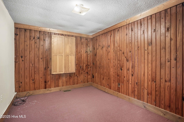 carpeted empty room with wooden walls and a textured ceiling