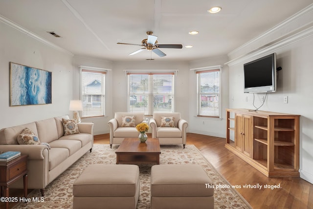 living room with ornamental molding, light wood-style flooring, visible vents, and a ceiling fan