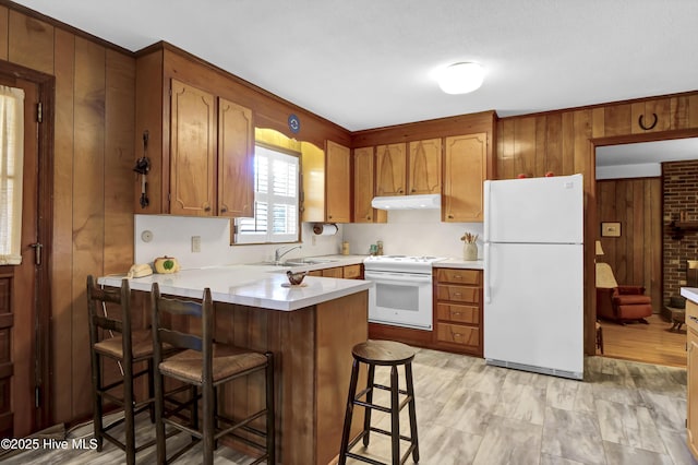 kitchen with sink, white appliances, a breakfast bar area, wooden walls, and kitchen peninsula