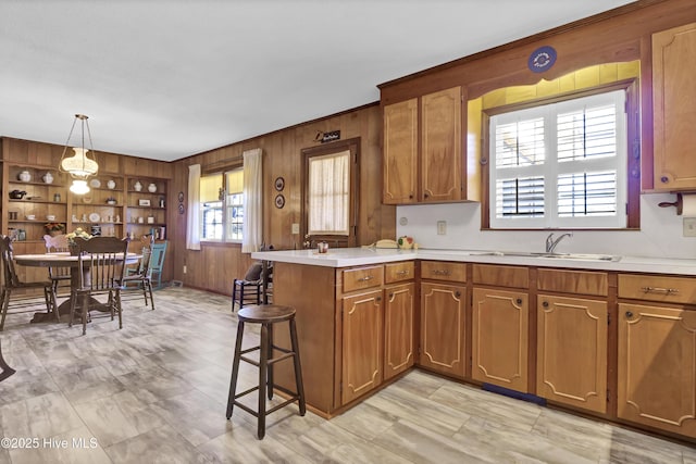 kitchen with a breakfast bar, sink, decorative light fixtures, wooden walls, and kitchen peninsula