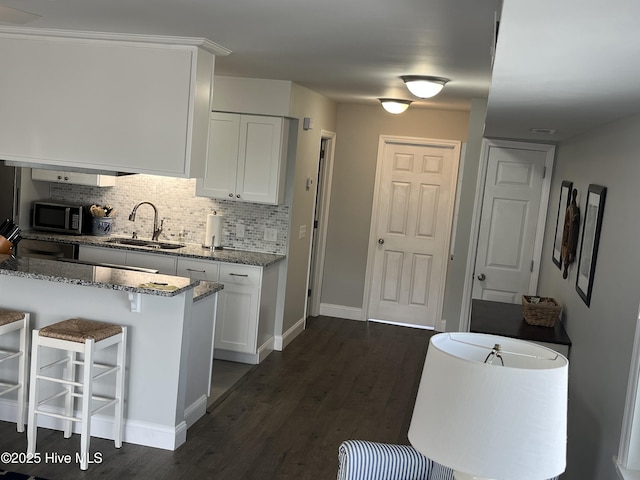 1801 Canal Dr Unit D14, Carolina Beach, NC 28428 - kitchen with a sink, stainless steel microwave, stone countertops, decorative backsplash, and white cabinetry