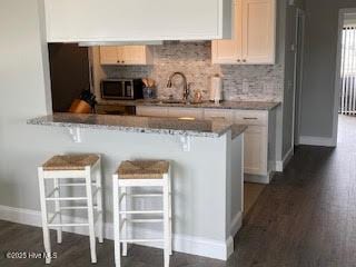 kitchen featuring decorative backsplash, stainless steel microwave, a sink, and a kitchen breakfast bar