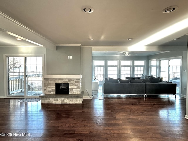 unfurnished living room with crown molding, a stone fireplace, dark hardwood / wood-style floors, and ceiling fan