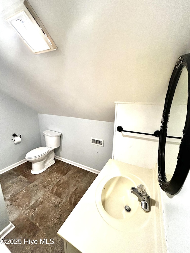 bathroom with lofted ceiling with skylight, vanity, and toilet