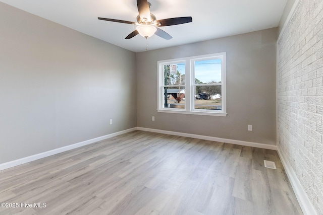 unfurnished room with ceiling fan, brick wall, and light wood-type flooring